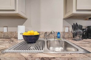 A kitchen with a stainless steel sink, a colander with lemons, a roll of paper towels, and a knife block.