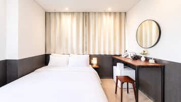 A hotel room with a bed, desk, chair, and a mirror.