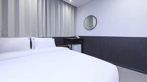 Hotellihuone, jossa on suuri sänky, yöpöytä, peili ja pieni työpöytä, jossa on puhelin.