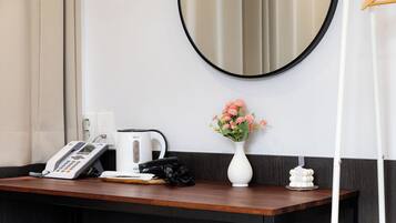 A hotel reception desk with a telephone, a coffee maker, a vase with flowers, and a mirror on the wall.
