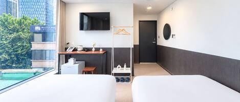 Habitación de hotel con dos camas, un escritorio con teléfono, televisor y vista a un edificio y árboles.