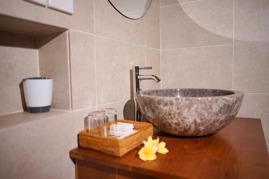 Un bany amb un lavabo de marbre, una safata de fusta amb sabó i una flor.