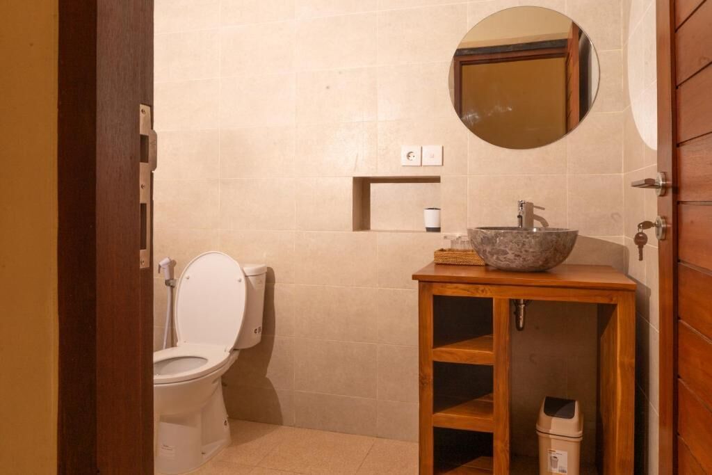 Ein Badezimmer mit Toilette, einem Waschbecken mit Steinbecken, einem Holzkabinet und einem Spiegel an der Wand.