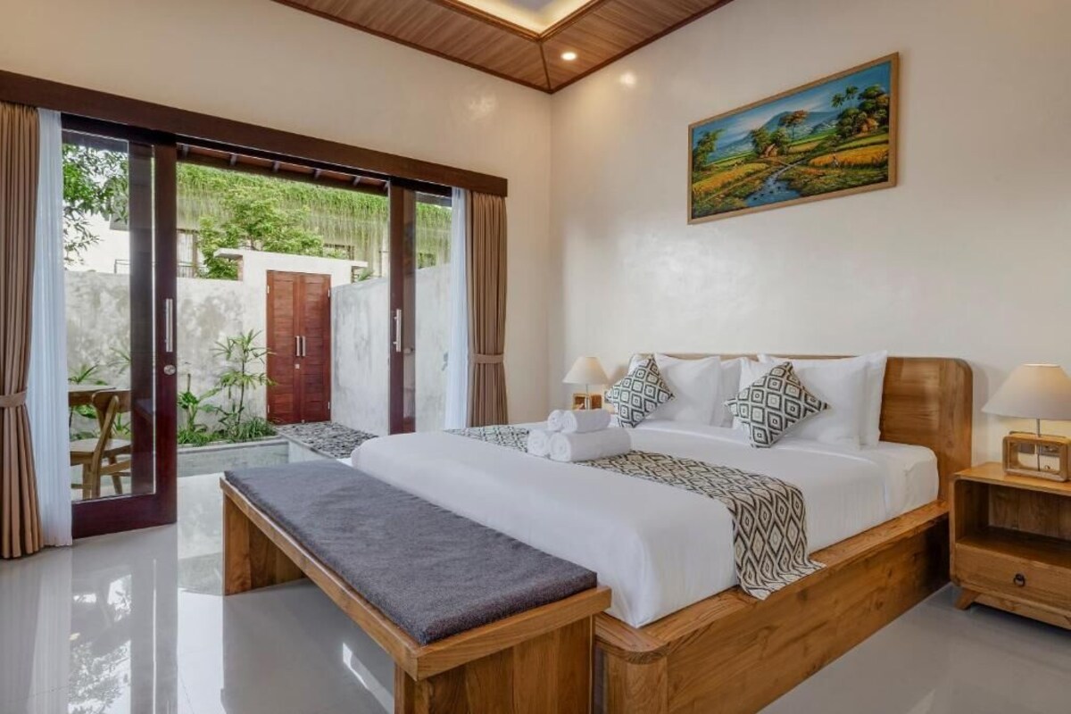 A bedroom with a large bed, a bench, a nightstand, and a painting on the wall.