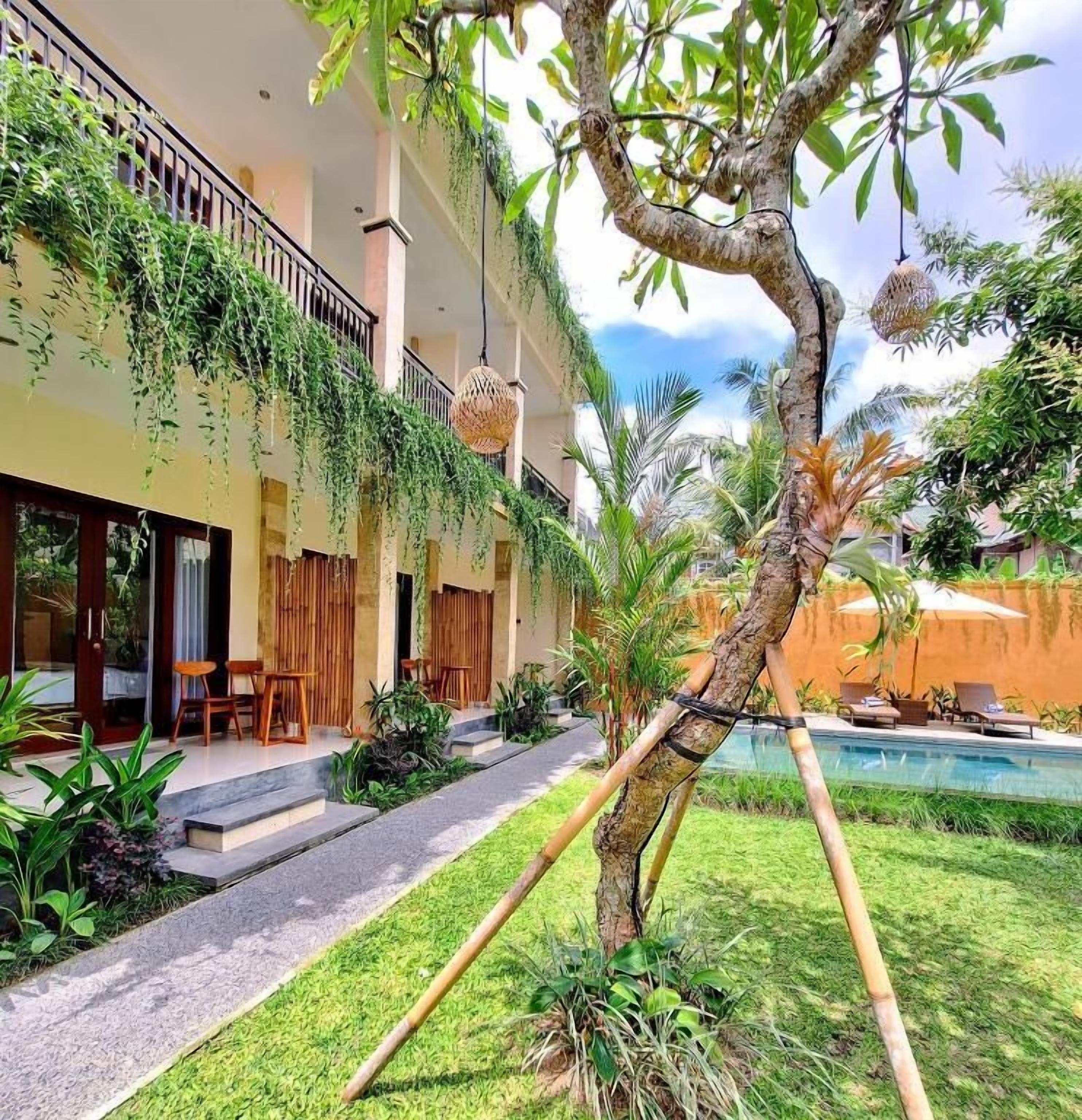 Un edificio con una zona de estar al aire libre techada, una piscina y un jardín cuidado con diversas plantas.