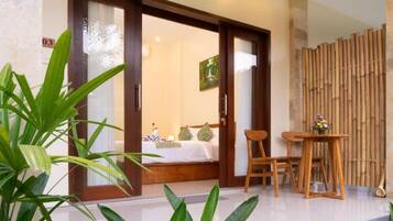 A hotel room with a bed, a chair, a table, and a bamboo screen.