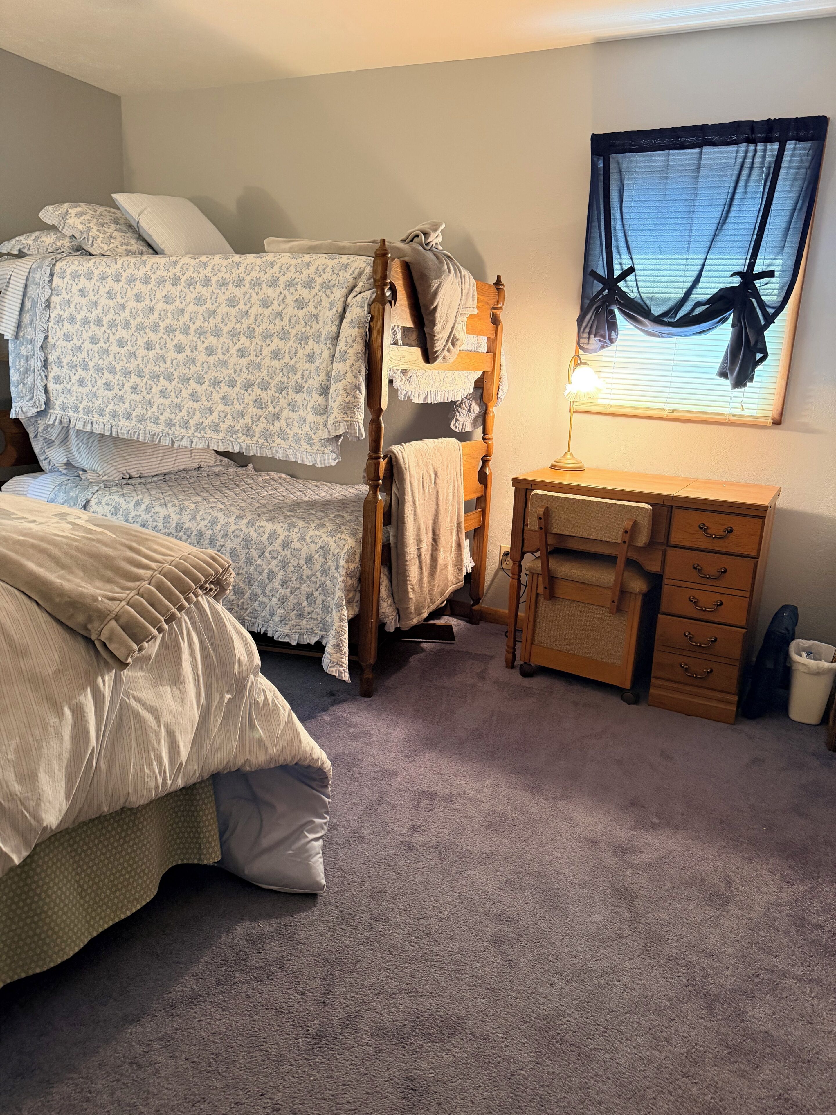 Une chambre avec un lit superposé, un bureau et une fenêtre avec des rideaux.