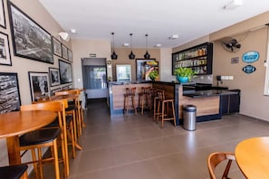 Ein Café mit Holztischen und -stühlen, einer Bar mit Regalen voller Flaschen und gerahmten Bildern an den Wänden.