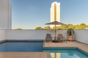 Ein Pool auf dem Dach mit gefliestem Boden, zwei Liegestühle, ein Tisch und ein Blumentopf.