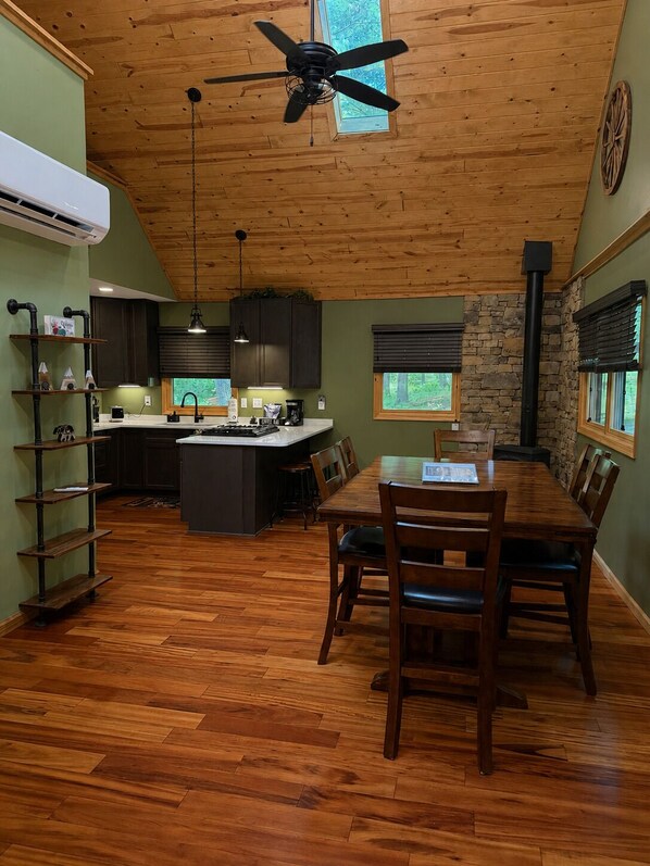 A kitchen with a central island, wooden flooring, a ceiling fan, and a stone wall.