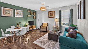 Een moderne woonkamer met een blauwgroene bank, een eethoek met een witte tafel en stoelen, een televisie en kunstwerken aan de muren.