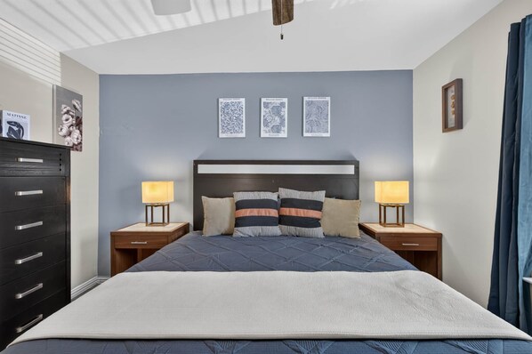 Ein Schlafzimmer mit einem Bett, zwei Nachttischen mit Lampen, einer Kommode und drei gerahmten Kunstwerken an der Wand.
