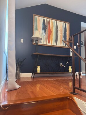 Eine Treppe führt zu einer Empore mit einer dunkelblauen Wand, einem farbenfrohen abstrakten Gemälde, einer Lampe und einer Vase auf einem Konsolentisch.