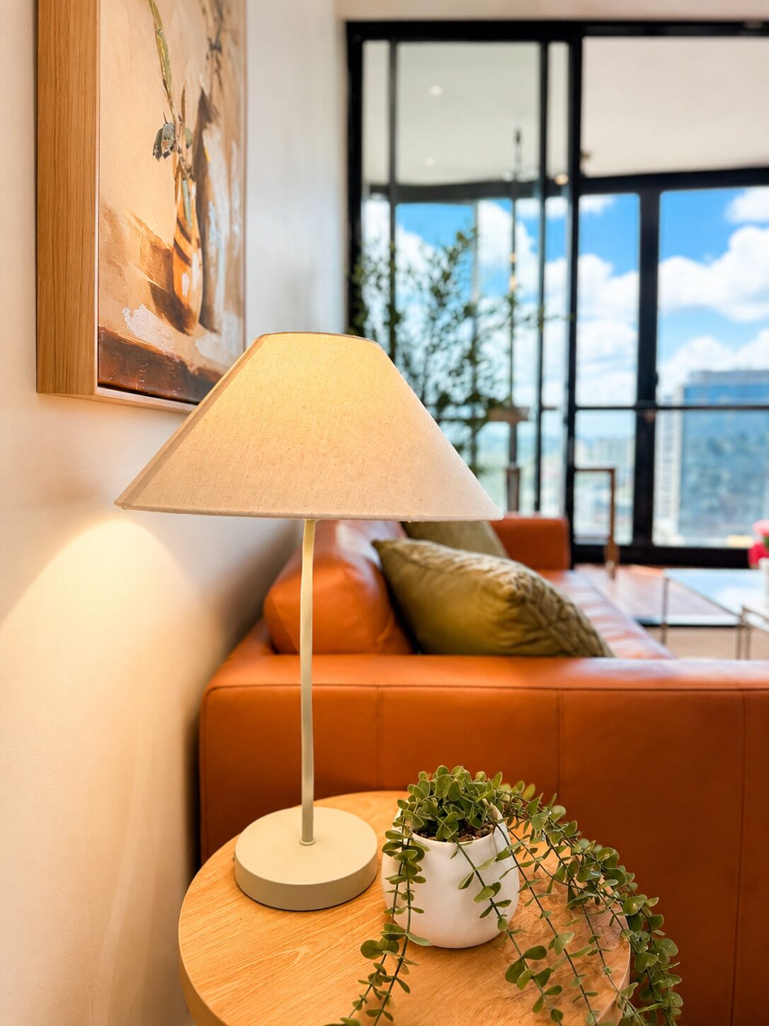 A modern living room with a sofa, a lamp, and a potted plant on a wooden table.