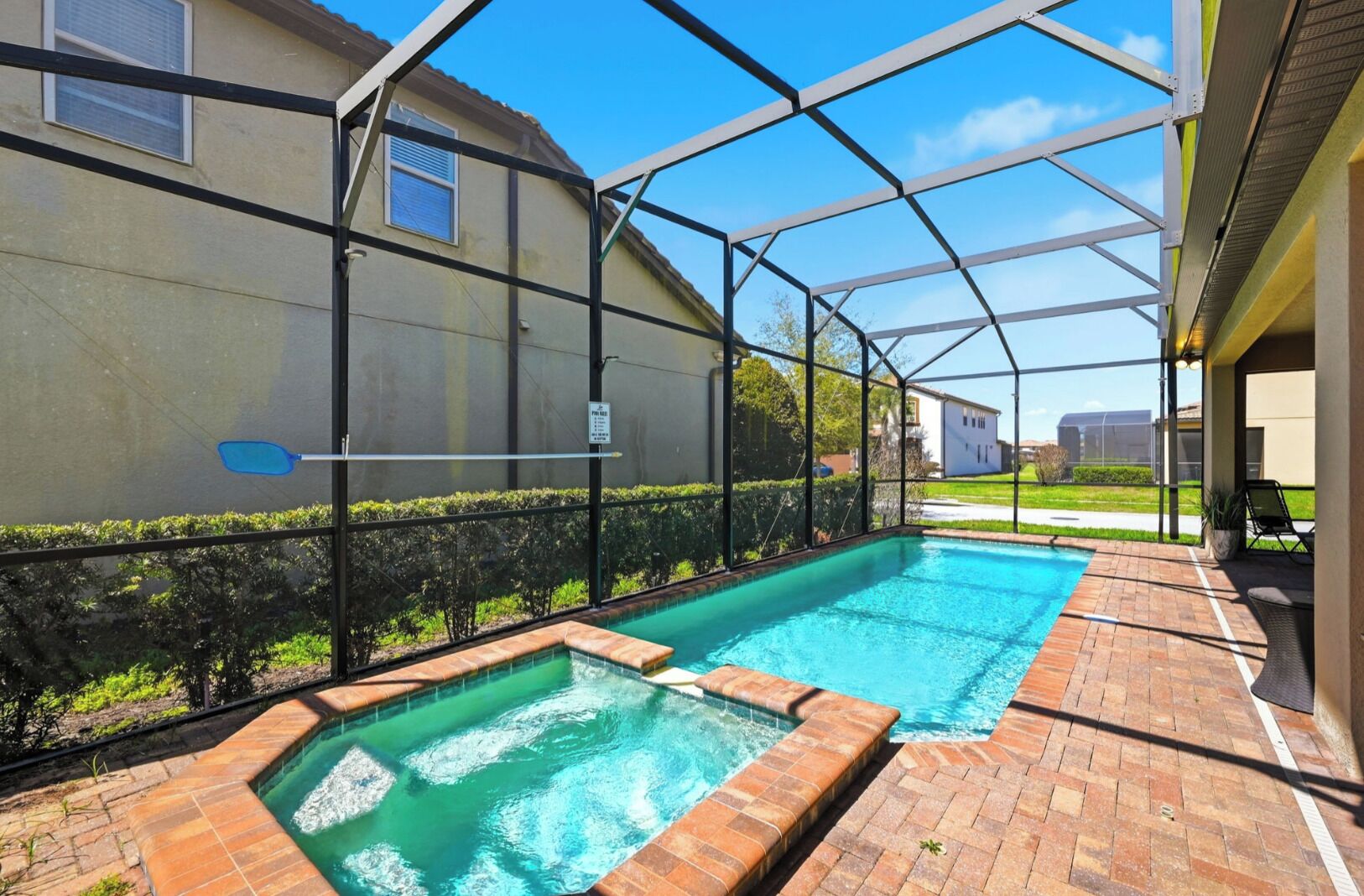 Une piscine entourée d’une enceinte en verre, bordée d’une terrasse en briques et d’une clôture en métal.