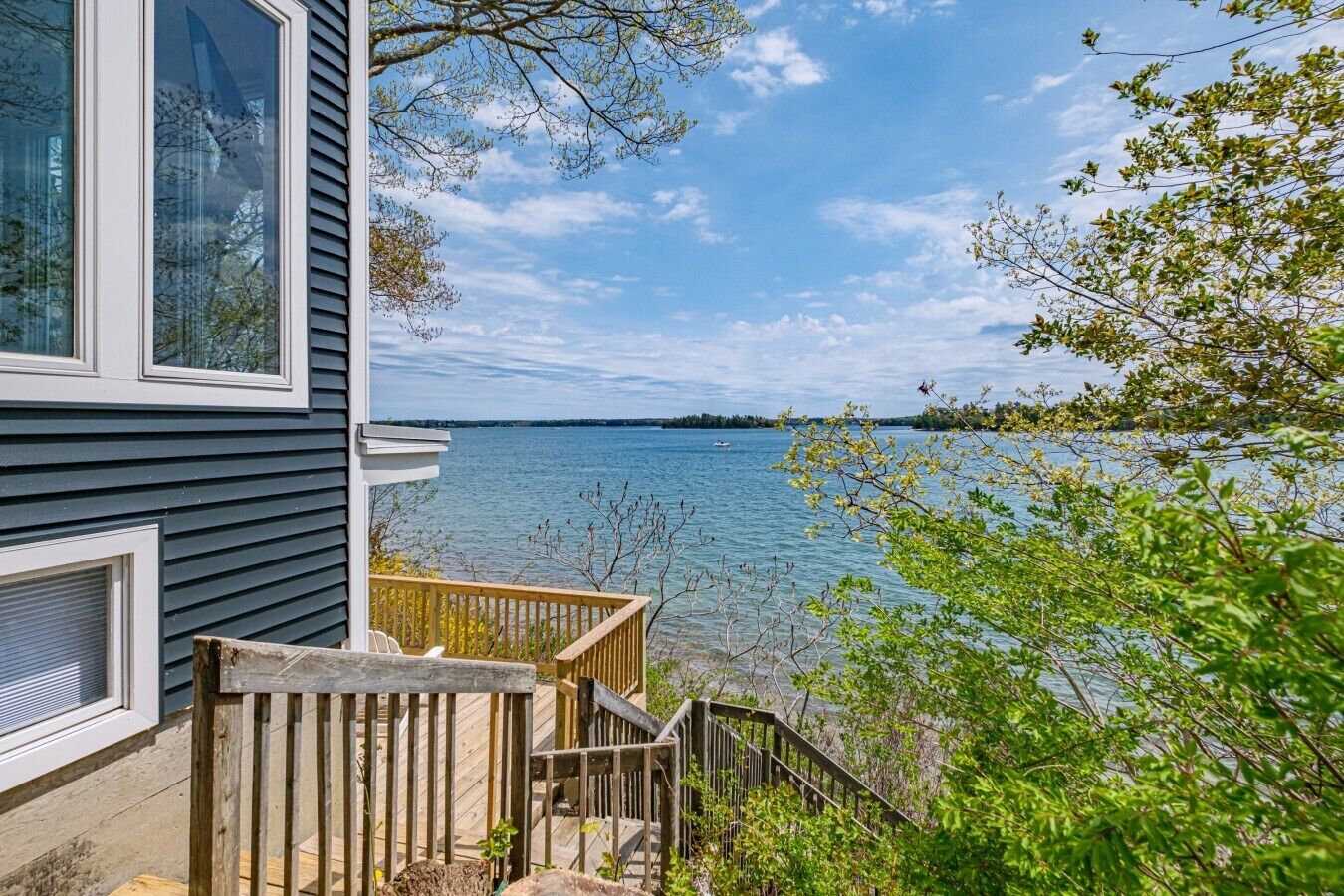A house with a view of a lake, a wooden deck, and a staircase leading to the deck.