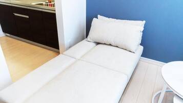 A small, single-bed room with a kitchenette, a white mattress, and a blue wall.