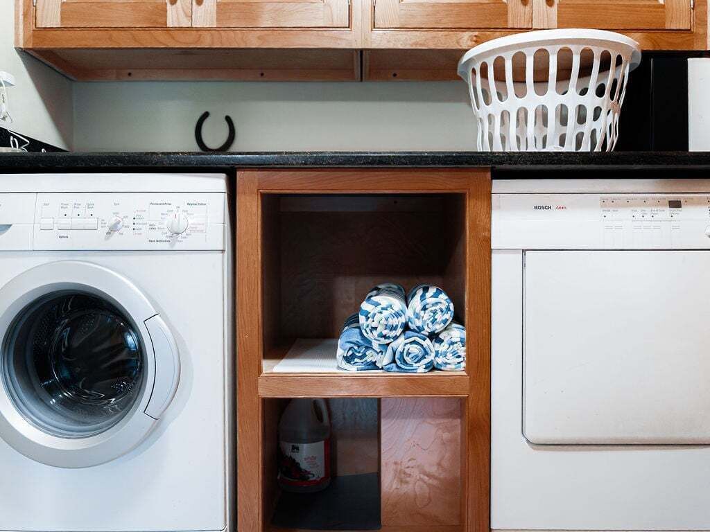 Une cuisine compacte équipée d’un lave-linge, d’un lave-vaisselle et d’une étagère en bois où sont rangées les serviettes.