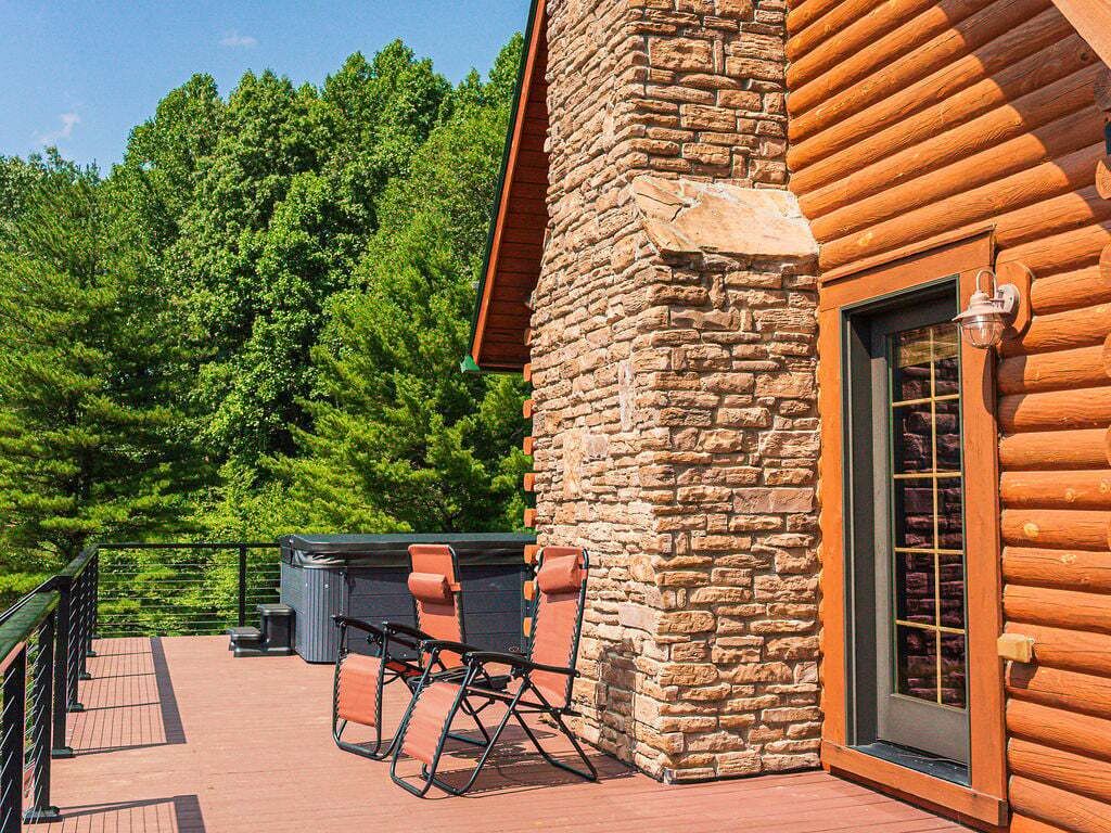Une cabane en rondins avec une cheminée en pierre, une terrasse avec des chaises et une vue sur une forêt dense.