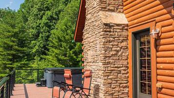 Une cabane en rondins avec une cheminée en pierre, une terrasse avec des chaises et une vue sur une forêt dense.