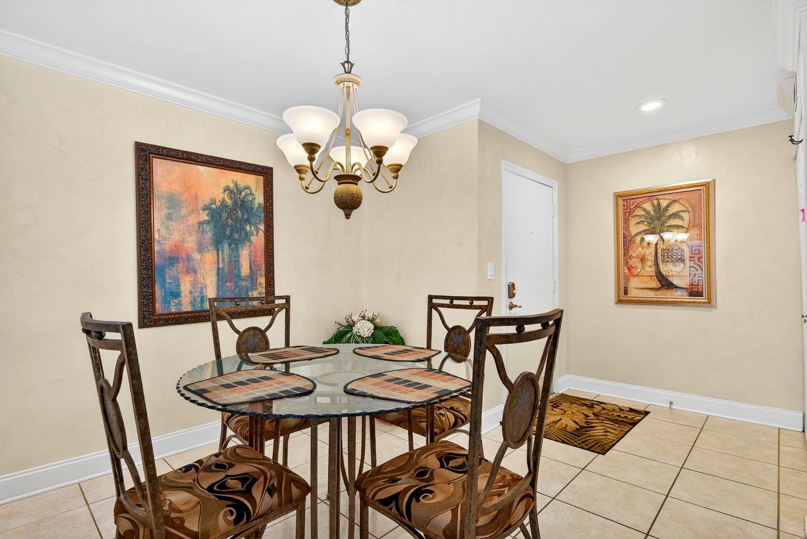 A dining area with a round table, chairs, a chandelier, and wall art.