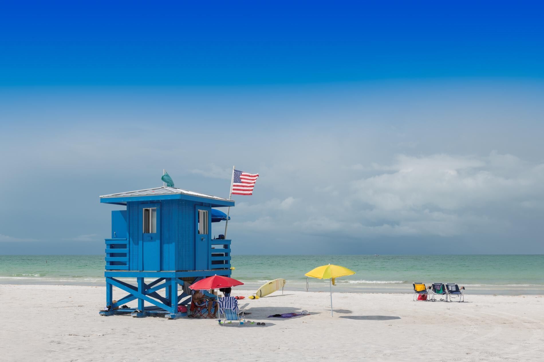 Une tour de surveillance avec un drapeau, des chaises de plage et des parasols, sur une plage de sable.