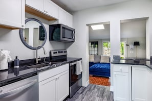 A compact kitchen with white cabinets, a microwave, a stove, and a sink.