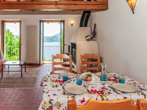 Uma sala de jantar com mesa posta para dois, uma cadeira de madeira, um sofá e vista para o exterior.