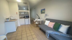 En kompakt opholdsstue med tekøkken, spiseplads og en sofa med mange puder.