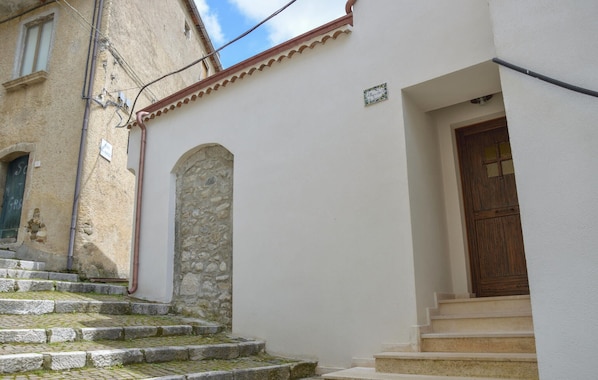 A building with a stone archway, a wooden door, and a set of stone steps leading to a white-walled entrance.