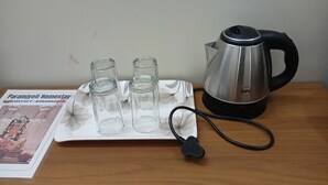 Una mesa con una tetera, tres vasos y un adaptador de corriente.