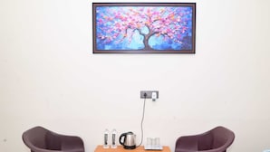 Una habitación con una mesa de madera, dos sillas de plástico, un cuadro de un árbol y un enchufe con un tapón.