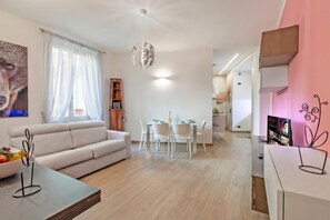 A modern living room with a sofa, dining table, and chairs. There is a chandelier, a TV, and a poster on the wall. - Charme Nest | Luxury Suite Milan - Isola, Milano, Italy (Milano)