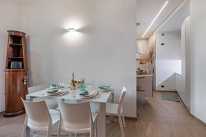 A modern dining area with a white table set for four, a wooden cabinet, and a kitchen in the background. - Charme Nest | Luxury Suite Milan - Isola, Milano, Italy (Milano)