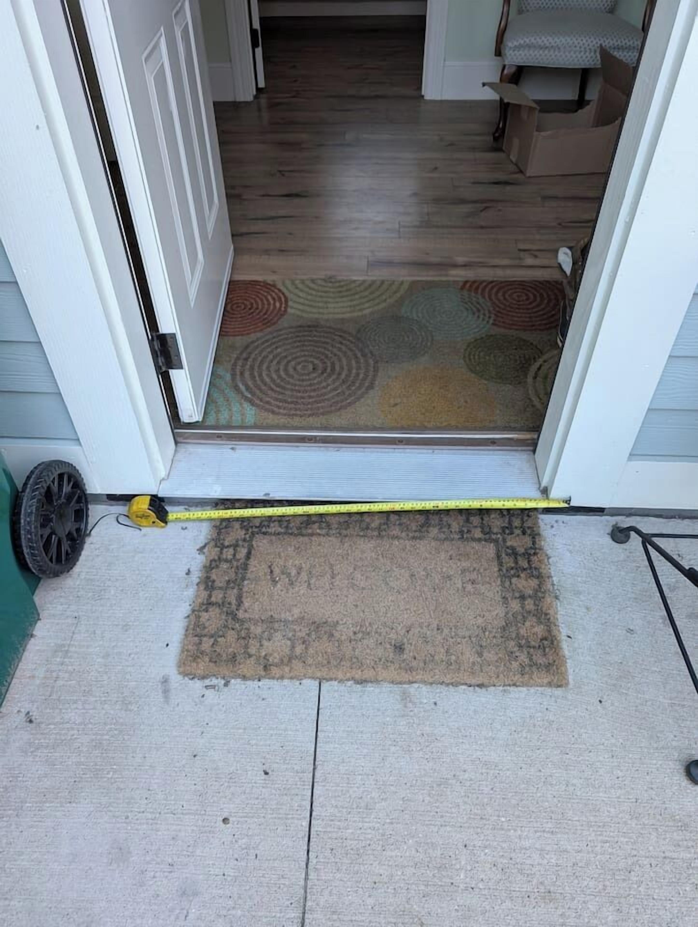 A doorway leading to a room with a patterned rug and a measuring tape on the floor.
