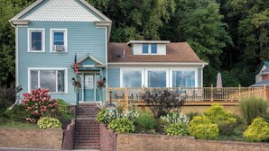 A two-story house with a front porch, a small deck, and a brick retaining wall. - Riverview, 5BR, Hot tub, Fireplace, Arcade Game (Minneiska)