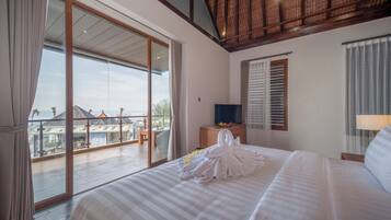 A hotel room with a large bed, a TV, a wooden nightstand, and a balcony with a view of the resort.