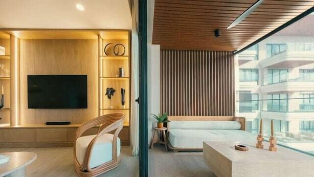 A modern living room with a flat-screen TV, a sofa, a coffee table, and a large window offering a view of buildings.