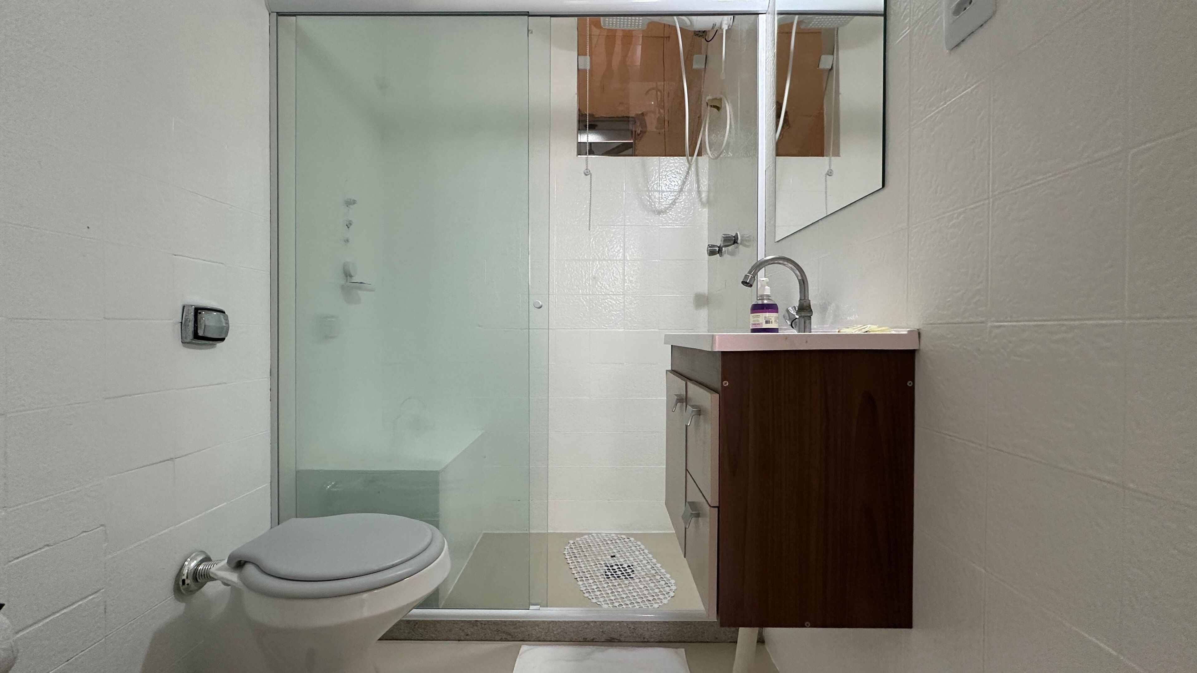A bathroom with a toilet, a glass shower enclosure, a sink with a mirror, and a wooden cabinet.