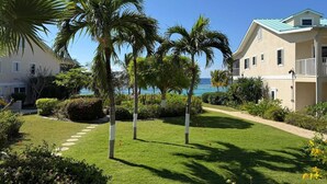A hotel with a well-maintained lawn, palm trees, and a view of the ocean. - Cayman Beach Escape - luxury ground floor 2BR (Savannah)