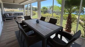 A covered outdoor dining area with a table and chairs, a sofa, and a view of a landscaped garden. - Cayman Beach Escape - luxury ground floor 2BR (Savannah)