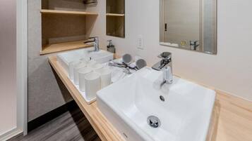 Un baño moderno con un lavamanos grande de color blanco, un espejo y un estante con artículos de aseo.