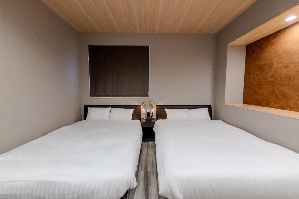 A hotel room with two single beds, a large window, and a wooden ceiling.
