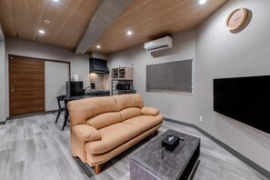 A modern living room with a sofa, a coffee table, a TV, and a dining area with chairs.