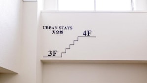 Una pared con una escalera que conduce a los pisos 4 y 3, con la etiqueta 'URBAN STAYS 天文館'.