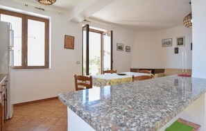 Une cuisine dotée d’un plan de travail en granit, de chaises en bois, d’une table à manger et d’un réfrigérateur.