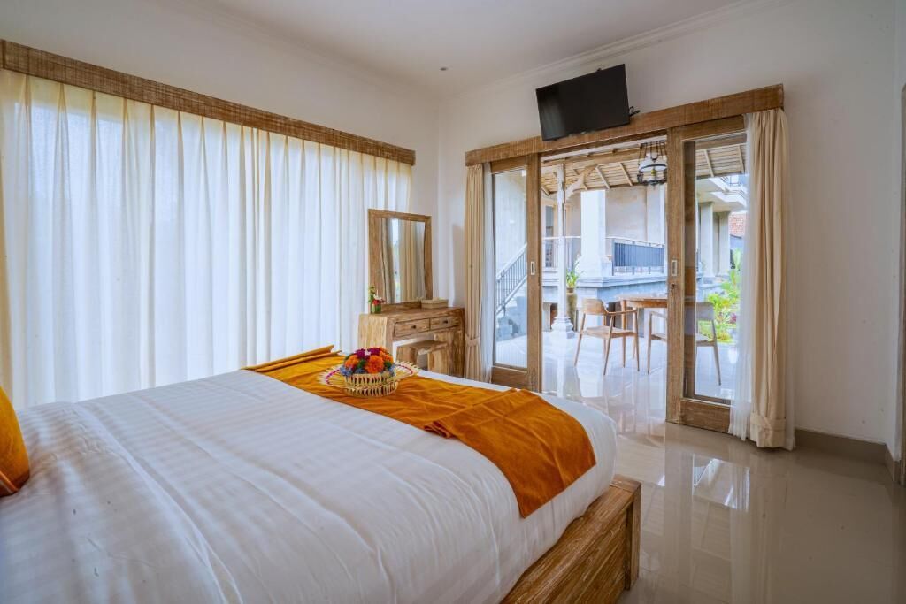 A hotel room with a bed, a wooden dresser, a television, and a balcony with a table and chairs.