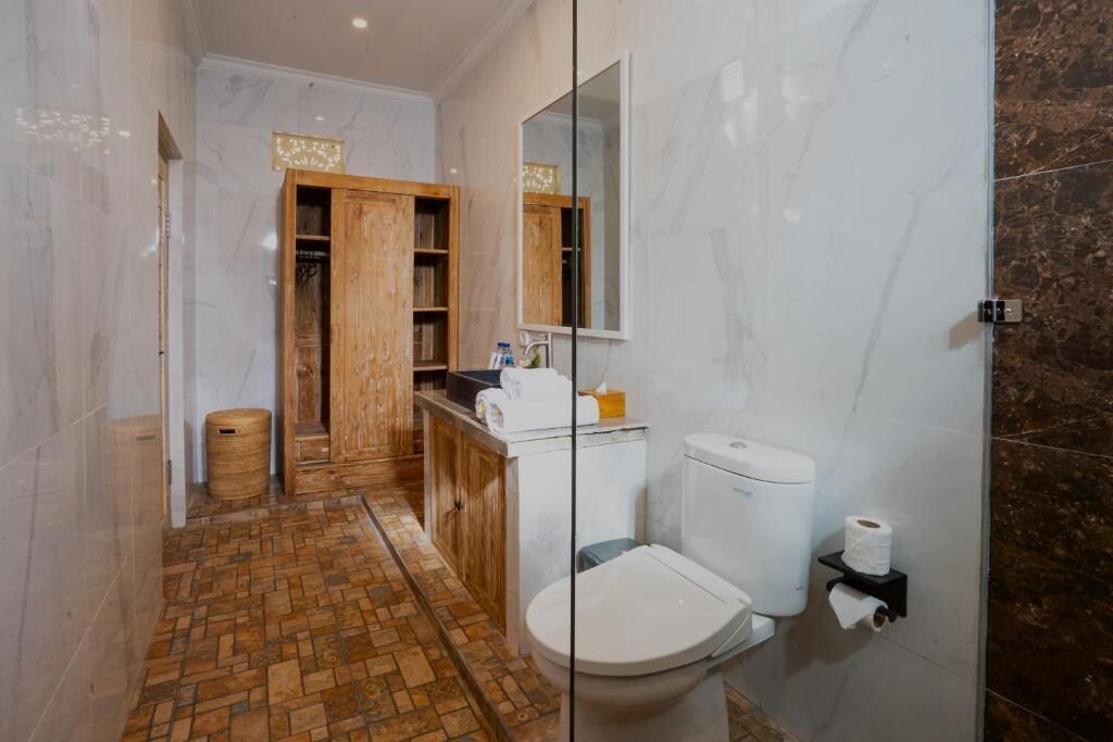 A bathroom with a toilet, a sink, a mirror, and a wooden cabinet.