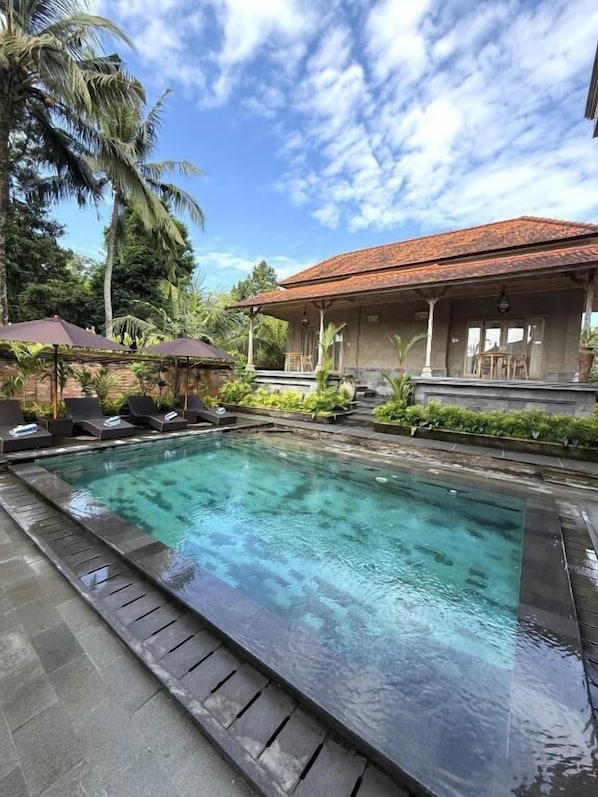 Uma piscina com espreguiçadeiras, área de estar coberta e um edifício com telhado em azulejos.