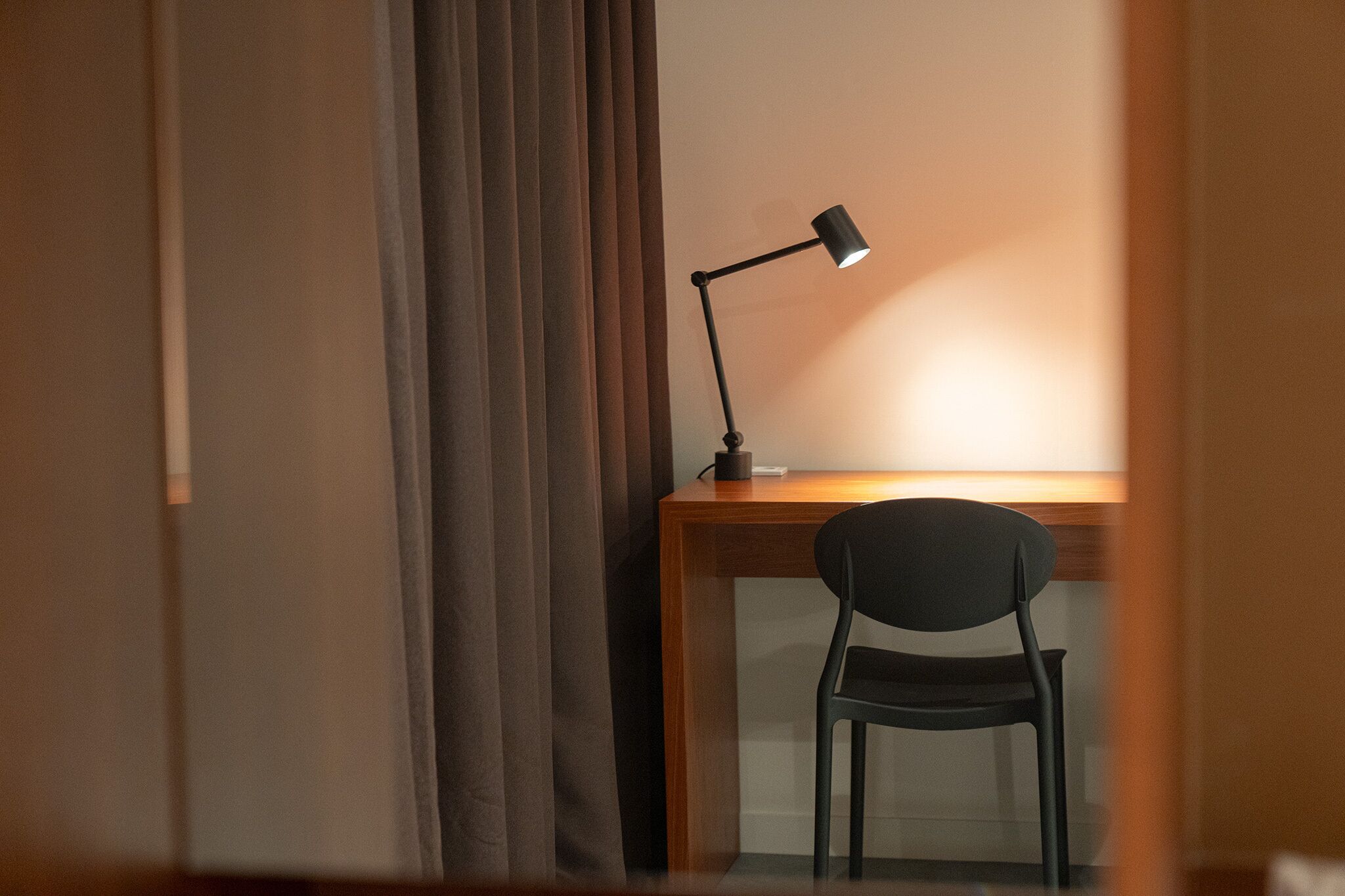 A room with a desk, a chair, a lamp, and a curtain.